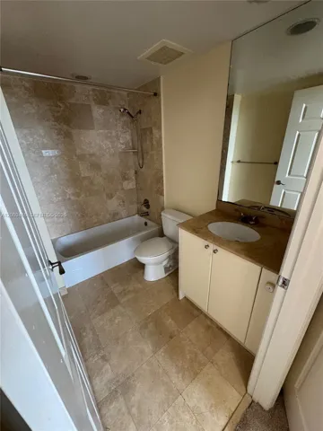 Guest Bathroom featuring natural stone tile flooring and tub surround, vanity with an integrated oval sink
