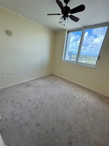 2nd bedroom again Room featuring large-scale windows with exterior cityscape, carpeted flooring, and a ceiling-mounted light fixture with integrated fan