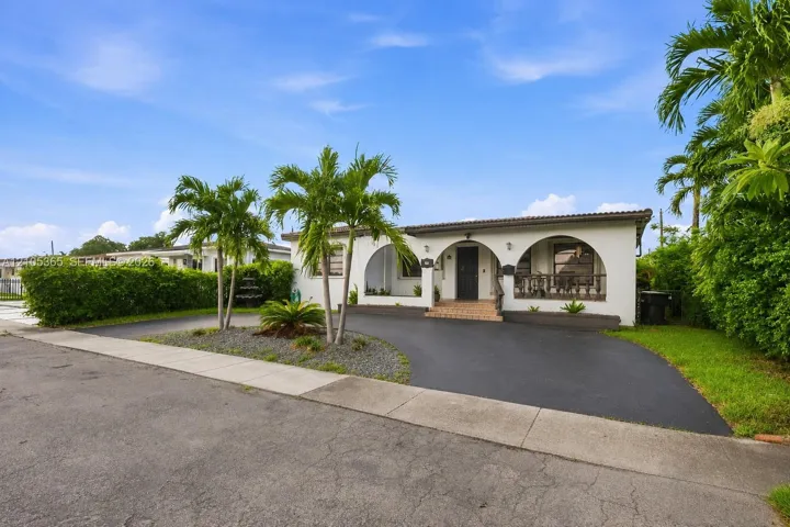 White stucco exterior with arched entryways, dark tile roof, paved driveway, and mature palm trees