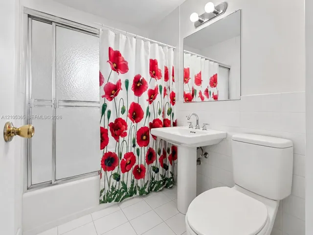 White tiled flooring, pedestal sink, wall-mounted mirror, and a tub with sliding glass doors