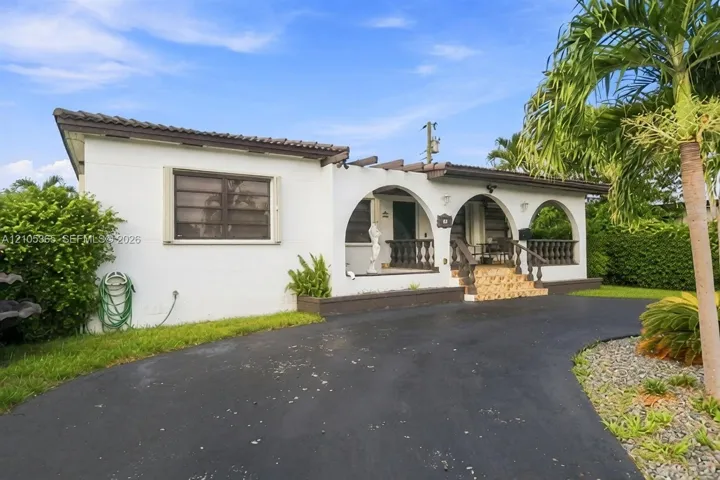 Arched front porch with balustrade railings, a curved asphalt driveway, and mature palm trees