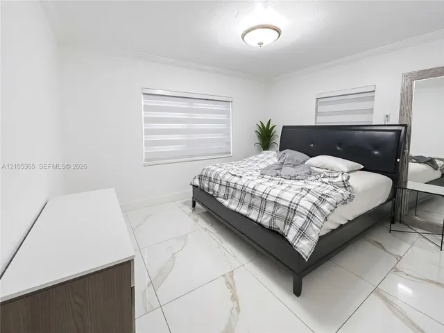 Spacious room featuring white tile flooring, crown molding, and two windows with blinds