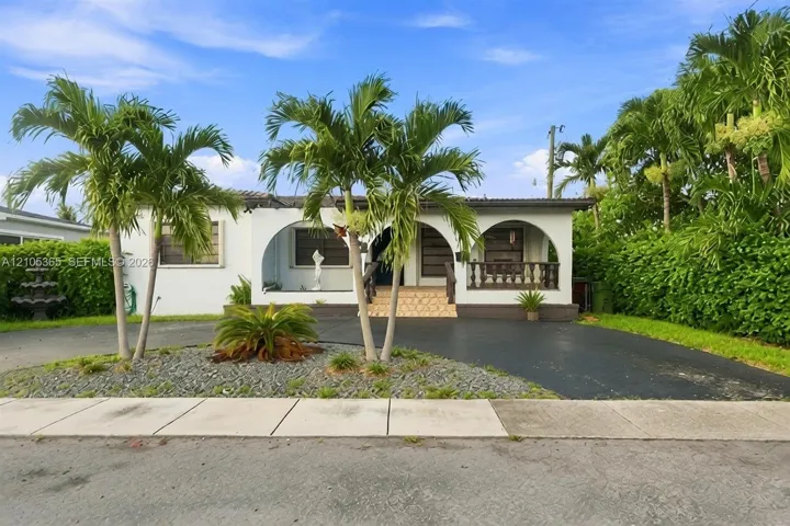 White stucco exterior with arched entryways, a tiled porch, and a dark paved driveway