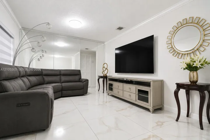 Polished tile flooring, crown molding, mirrored wall, and a media console with glass-front cabinets