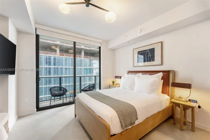 White walls, a ceiling-mounted light fixture, and a sliding glass door opening to a private balcony with metal railings