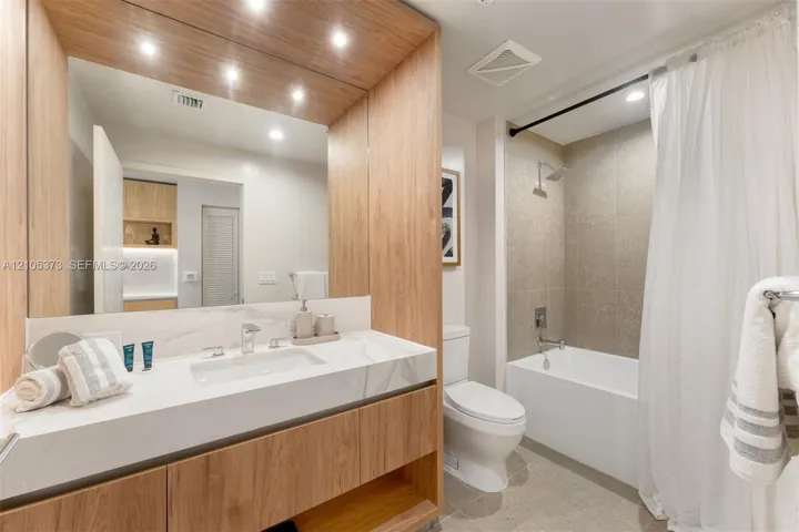 Bathroom featuring a wood-finish vanity, integrated rectangular sink, and a combination tub/shower with tiled walls