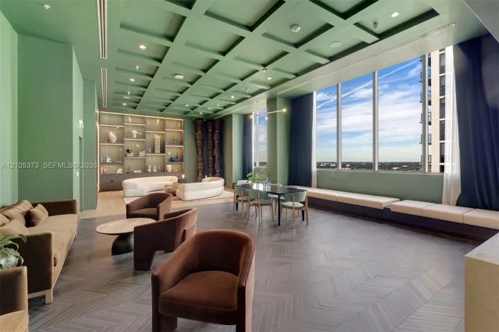 Spacious lounge area featuring a coffered ceiling, floor-to-ceiling windows, built-in shelving with integrated lighting, and herringbone pattern flooring