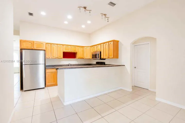 Kitchen featuring wood cabinetry, stainless steel appliances, dark countertops, and tile flooring