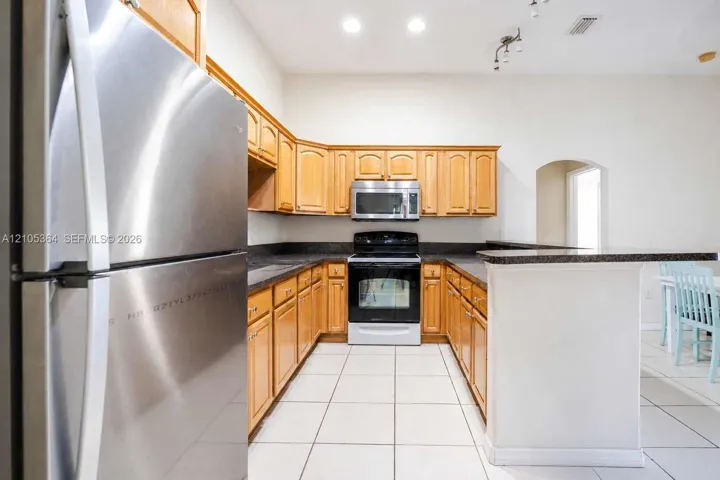 Kitchen with wood cabinetry, dark countertops, a stainless steel refrigerator, and a built-in microwave