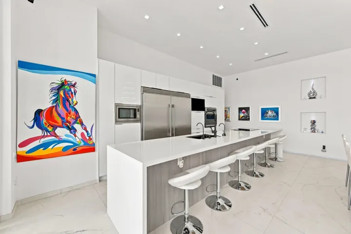 Modern kitchen featuring integrated stainless steel appliances, a large island with a waterfall countertop, recessed lighting, and built-in display niches