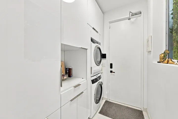 White glossy cabinetry with integrated hardware, stacked washer and dryer, and a fixed pane window