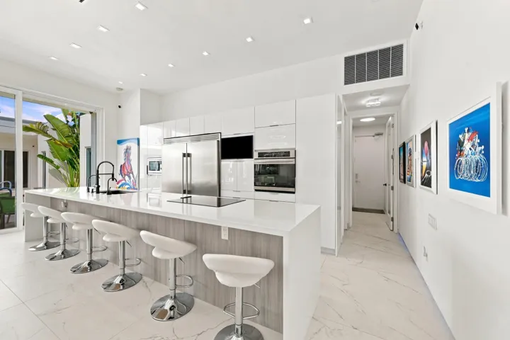 Contemporary kitchen featuring an oversized island with seating, stainless steel appliances, white cabinetry, a built-in cooktop, and large format tile flooring