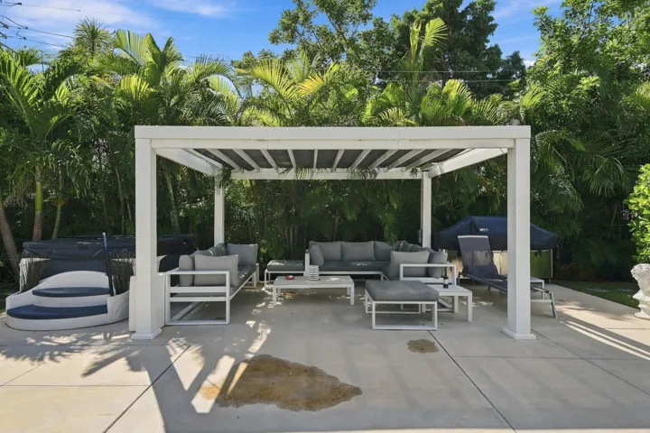 Expansive concrete patio featuring a white pergola structure with adjustable louvered panels
