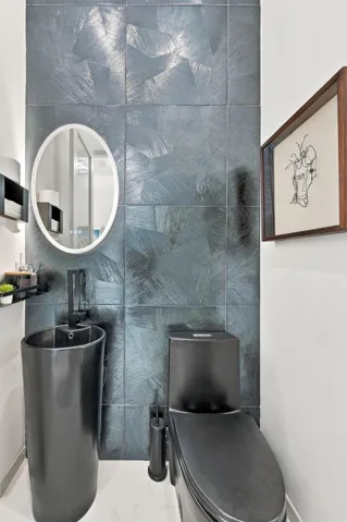 Textured wall tiling, pedestal sink with integrated faucet, contemporary black toilet, and oval-framed mirror