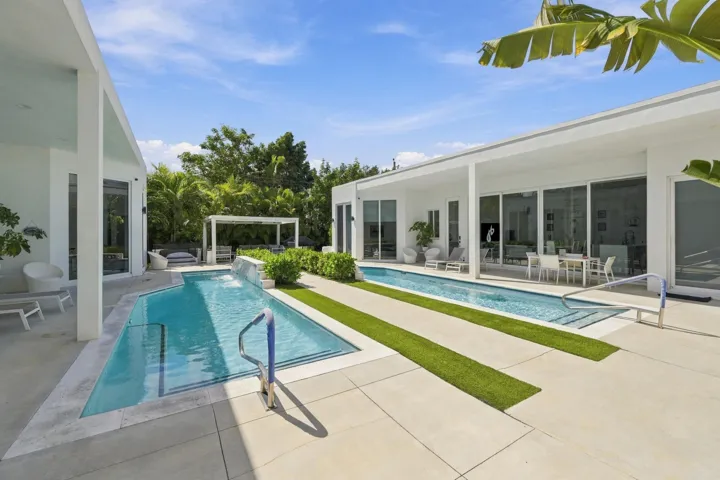Expansive outdoor area featuring two distinct pools, a white pergola, and concrete paver hardscaping with integrated turf strips