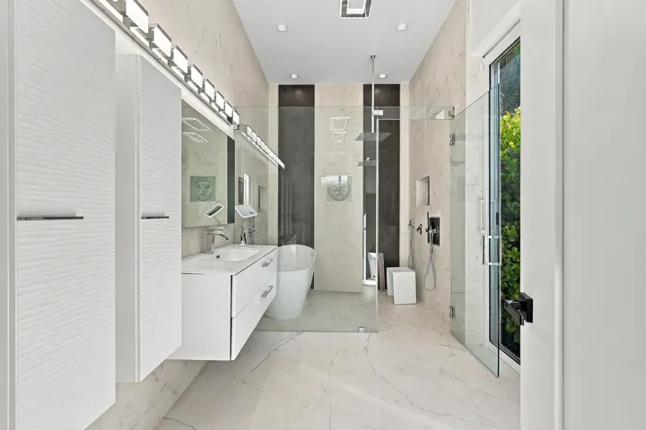 Floating vanity with integrated sink, glass-enclosed shower, freestanding tub, recessed lighting, and large format floor tiles