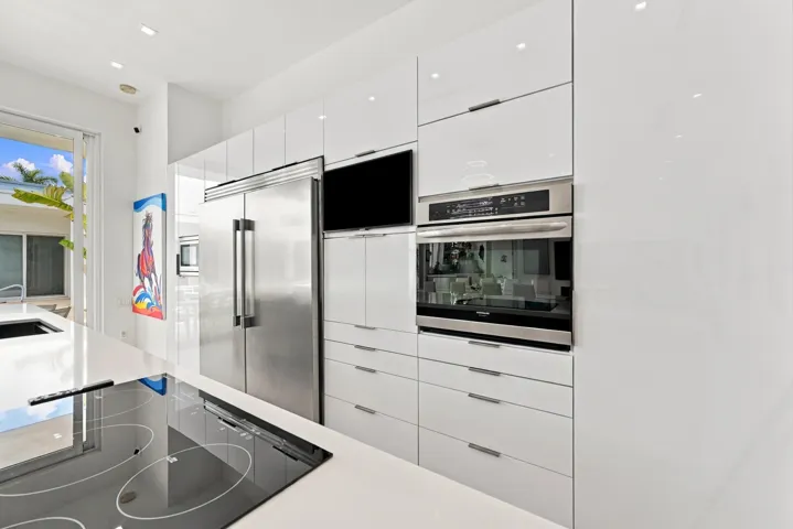 Sleek white cabinetry, integrated stainless steel appliances, and a built-in cooktop complement the kitchen's contemporary design