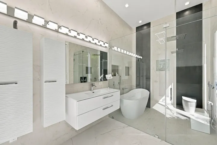 Freestanding soaking tub, glass-enclosed shower with dual shower heads, floating vanity with integrated sink, and dual built-in tall cabinets with textured fronts
