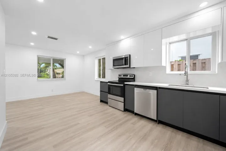 Kitchen featuring two-tone cabinetry, stainless steel appliances, light-toned wood-finish flooring, recessed lighting, and solid-surface countertops