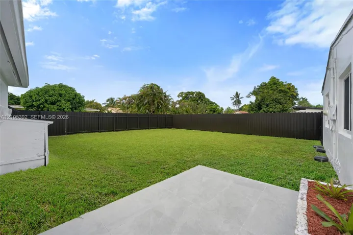 Expansive backyard featuring a large grass area, dark perimeter fencing, and a concrete patio