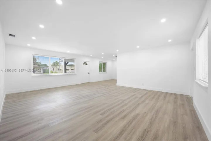 Spacious room with wood-finish flooring, white walls, multiple windows, and recessed lighting