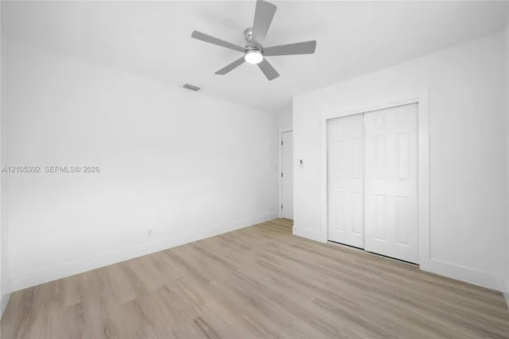 Light-toned wood-finish flooring, white walls, and a contemporary ceiling fan with integrated lighting