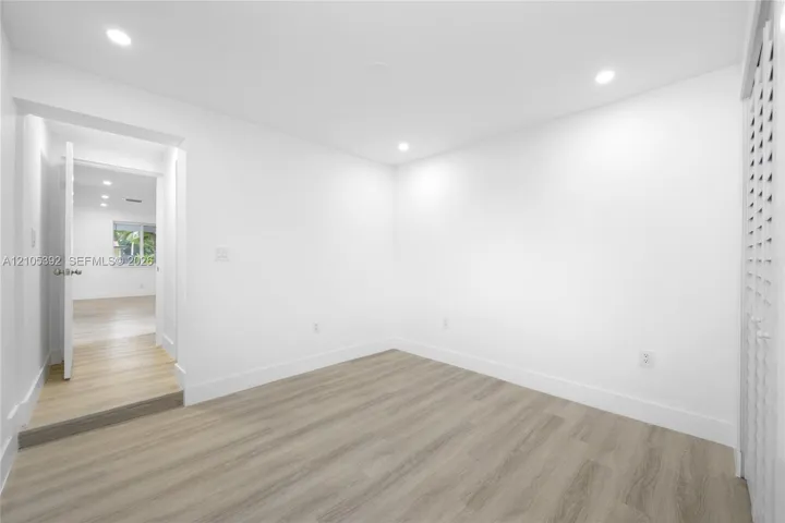 Recessed lighting, wood-finish flooring, white walls, and a louvered door
