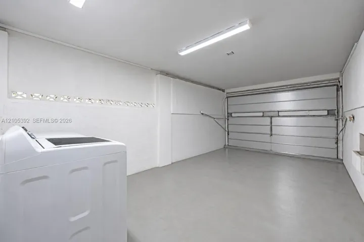 White walls, concrete flooring, fluorescent lighting, and a metal roll-up door