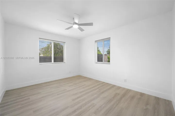 Bright interior with wood-finish flooring, two large windows, a ceiling fan with integrated lighting, and crisp white walls