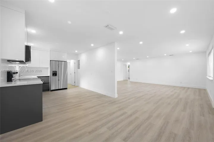 Wood-finish flooring throughout, recessed lighting, white walls, kitchen with white upper cabinetry, and stainless steel refrigerator
