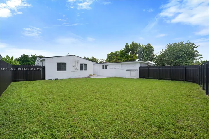 Expansive backyard with a manicured lawn, dark fencing, and a white stucco exterior