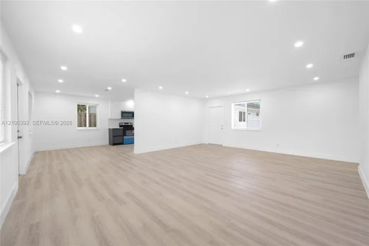 Spacious open-concept interior featuring light wood-finish flooring, recessed lighting, and crisp white walls