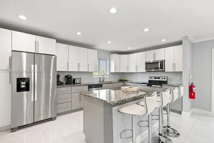 Kitchen featuring stainless steel appliances, granite countertops, white upper cabinetry, grey base cabinetry, and recessed lighting