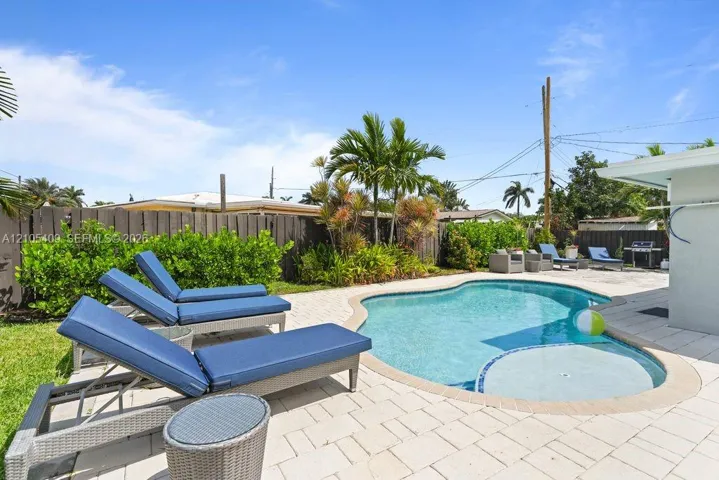 Freeform swimming pool with a spa, surrounded by paver decking, a wood privacy fence, and mature landscaping