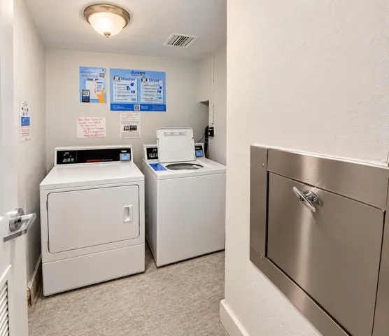 Laundry area with utility flooring, ceiling-mounted light fixture, and a wall-mounted stainless steel receptacle