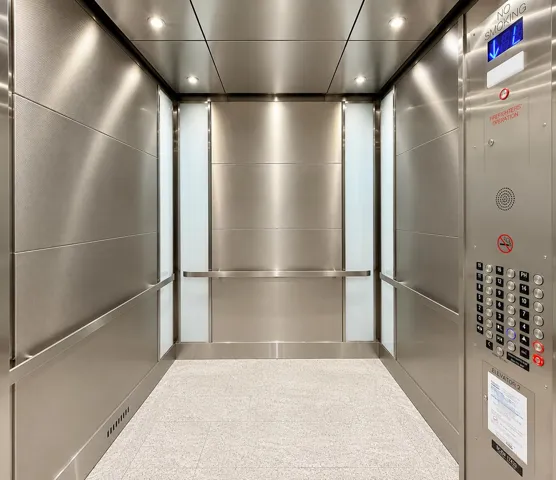 Stainless steel interior paneling, recessed ceiling lighting, a full-height control panel, light-colored flooring, and integrated handrails