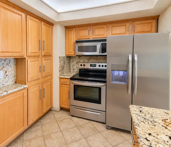 Kitchen featuring stainless steel appliances, wood cabinetry, stone countertops, stone backsplash, and tiled flooring