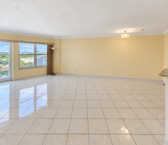 Expansive living area featuring large tile flooring, a wide window with city and green space scenery, and a semi-flush ceiling light fixture