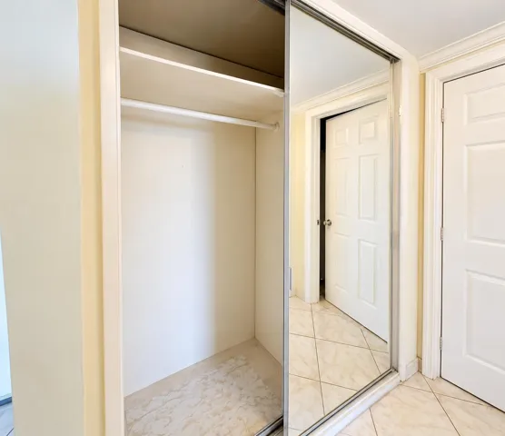 Built-in closet with hanging rod and upper shelf, featuring sliding mirrored doors and a light-toned tile floor