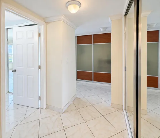 Tile flooring, crown molding, built-in sliding panel doors with wood-finish and frosted glass, mirrored closet doors, and flush-mount ceiling lights
