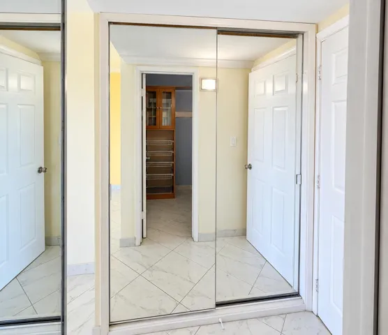 Mirrored sliding closet doors with white trim, white paneled doors, and white tile flooring