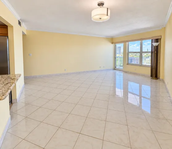 Spacious living area featuring polished tile flooring, crown molding, a built-in granite counter, and a large window with sliding glass door
