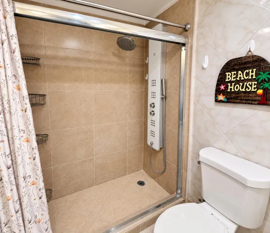 Glass-enclosed shower with a multi-function shower panel, rainfall shower head, and tiled walls