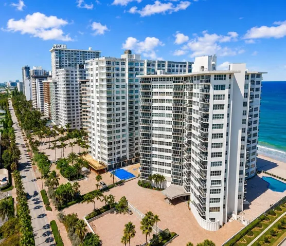 High-rise coastal building with multiple balconies, an adjacent swimming pool, and a dedicated entrance driveway