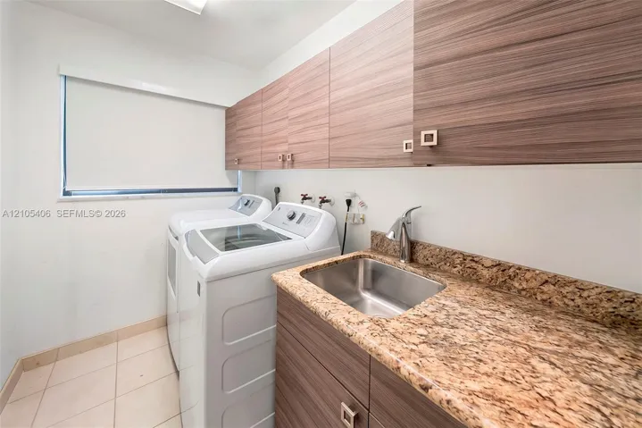 Laundry area featuring a utility sink, polished chrome faucet, stone-finish countertop, wood-finish cabinetry, and tiled flooring