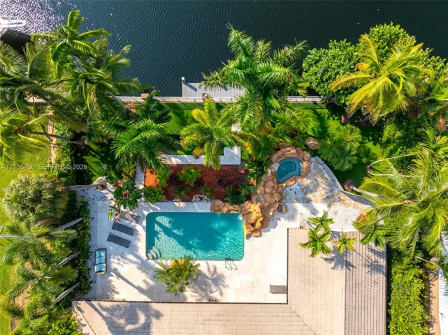 Waterfront property featuring a swimming pool, integrated spa, expansive paver patio, and lush tropical landscaping