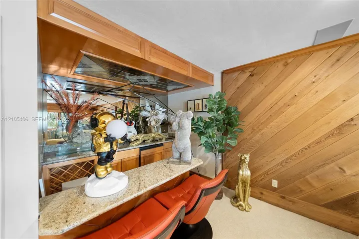 Built-in bar with wood cabinetry, mirrored backsplash, and stone countertop