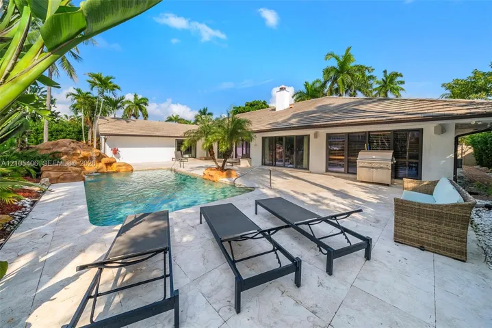 Outdoor space featuring a swimming pool with a rock waterfall, extensive paved patio, and tropical landscaping