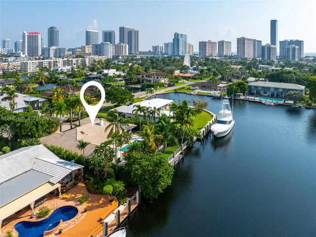 Waterfront property featuring a private boat dock, lush landscaping with mature palm trees, a swimming pool, and a tiled roof, with a city skyline in the background