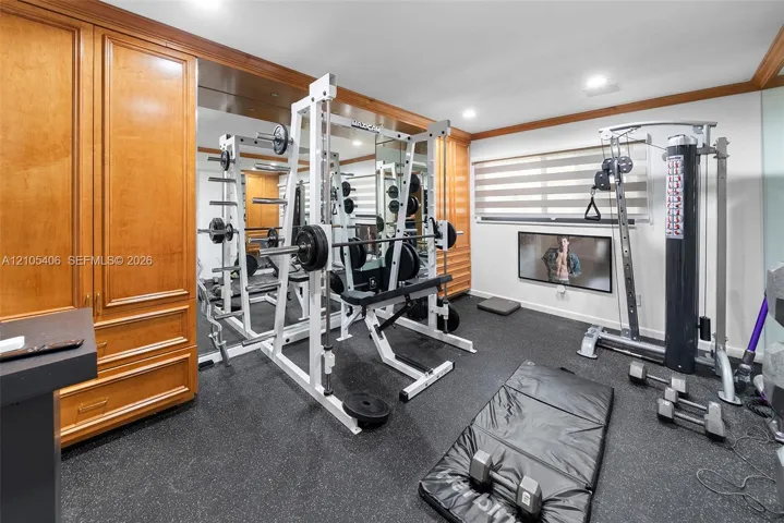 Custom built-in cabinetry, full-wall mirror, window with horizontal blinds, ceiling-mounted recessed lighting, and rubberized flooring